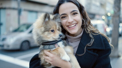 Wall Mural - Young hispanic woman with dog smiling confident standing at street