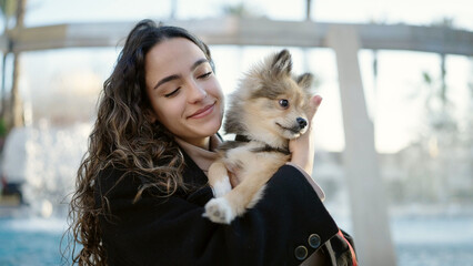 Wall Mural - Young hispanic woman with dog smiling confident standing at park