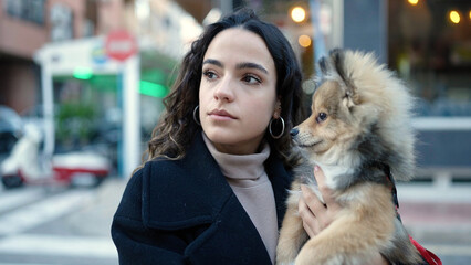 Young hispanic woman with dog standing with serious expression at street