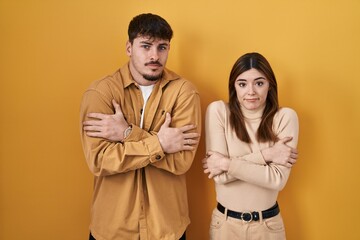 Canvas Print - Young hispanic couple standing over yellow background shaking and freezing for winter cold with sad and shock expression on face