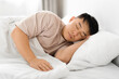 Tired middle aged asian man asleep, resting peacefully in bed