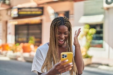 Canvas Print - African american woman using smartphone with surprise expression at street