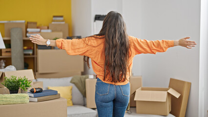 Young beautiful hispanic woman standing backwards with arms open at new home