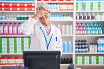 Canvas Print - Middle age woman with tattoos working at pharmacy drugstore smiling and laughing with hand on face covering eyes for surprise. blind concept.