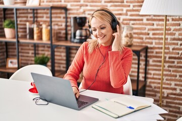 Canvas Print - Young blonde woman listening to music sitting on table at home