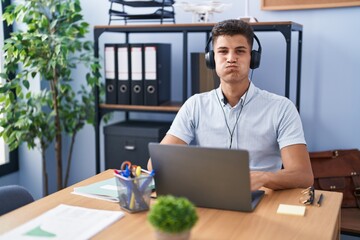 Sticker - Young hispanic man working at the office wearing headphones puffing cheeks with funny face. mouth inflated with air, crazy expression.