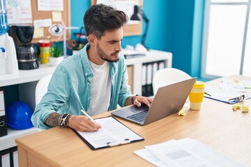 Sticker - Young hispanic man business worker using laptop writing on document at office