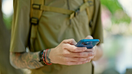 Sticker - Young hispanic man tourist wearing backpack using smartphone at park