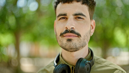 Wall Mural - Young hispanic man wearing headphones with relaxed expression at park