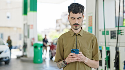 Wall Mural - Young hispanic man using smartphone with serious expression at petrol station