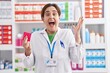 Brunette woman working at pharmacy drugstore holding condom celebrating victory with happy smile and winner expression with raised hands