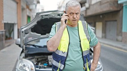 Poster - Middle age grey-haired man talking on smartphone with insurance for car breakdown at street