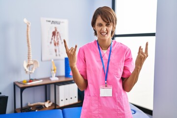 Poster - Brunette woman working at rehabilitation clinic shouting with crazy expression doing rock symbol with hands up. music star. heavy concept.