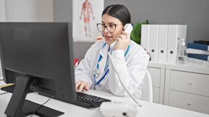 Sticker - Young hispanic woman doctor using computer speaking on telephone at clinic