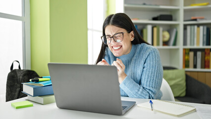 Poster - Young hispanic woman student using laptop celebrating at library university