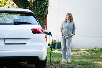 Sticker - Woman next to a charging electric car in the yard of a country house