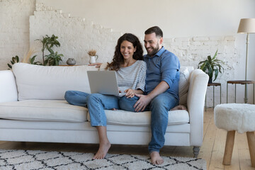 Wall Mural - Cheerful attractive couple of homeowners enjoying leisure, Internet communication at home, shopping online, making video call, watching movie, interactive TV. Full length