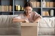 © fizkes - Woman sit on couch feels happy received parcel gift or ordered goods in internet websites opening big carton box hold it on lap, convenient service, quick shipping at home, transport delivery concept