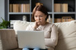 © fizkes - Middle-aged woman sit on sofa holds on lap laptop looks at pc screen feels concerned, need repair or help with program, older generation having difficulties and barriers of modern tech devices concept