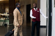 © AnnaStills - African American doorman calling the elevator to the guest while they standing in the hall