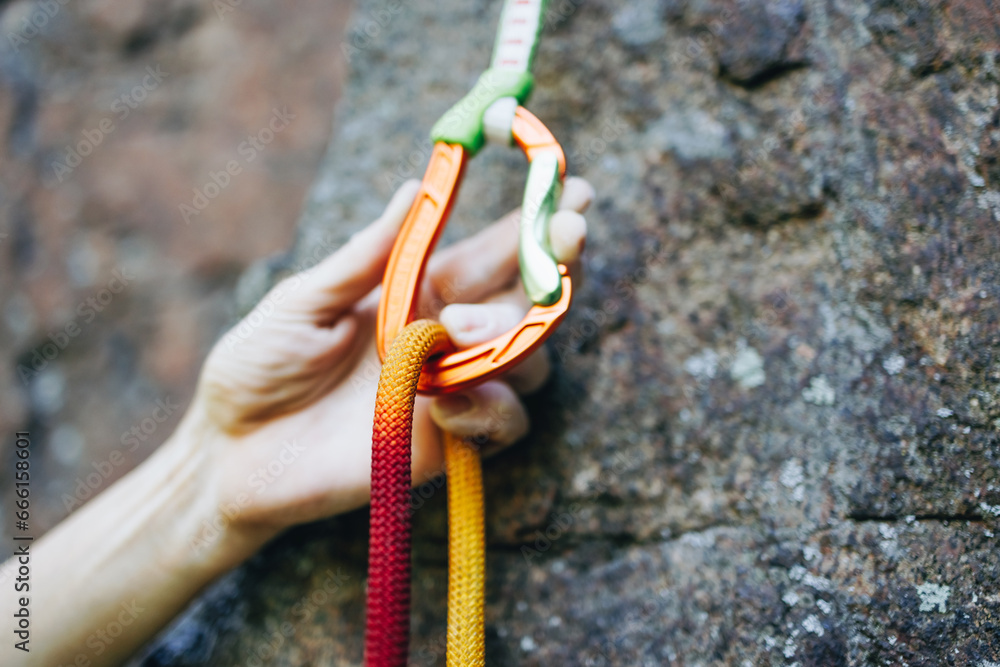 Close up of rock climber hand clipping rope in a quick draw caribener ...