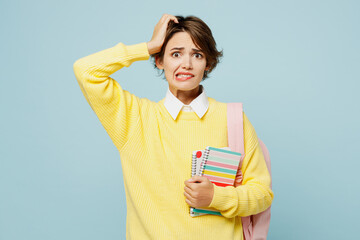 Wall Mural - Young worried shocked mistaken confused woman student wear casual clothes yellow sweater backpack bag hold books scratch head isolated on plain blue background. High school university college concept.