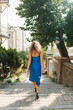 © Mila - A slender girl with long hair in a blue dress walks along the street among the old buildings of the ancient city.A beautiful woman in an evening dress posing against the background of old architecture