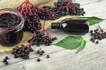 Wall Mural - Black elderberry fruit on vintage wooden board, Sambucus. Branches of elderberry with green leaves, elderberry jam, syrup and confiture. European black elderberry. Alternative medicine and lifestyle.