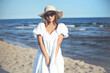 © rogerphoto - Happy smiling blonde woman is posing on the ocean beach with sunglasses and a hat