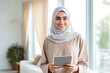 © VisualProduction - Arabic happy woman using tablet on couch in smart home. Modern home innovation and technology. Using a mobile tablet to control smart home.