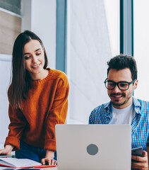 Wall Mural - positive smiling man and woman near working place with laptop cooperating in office