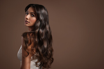 Wall Mural - Gorgeous woman with shiny wavy hair on brown background, space for text. Professional hairstyling