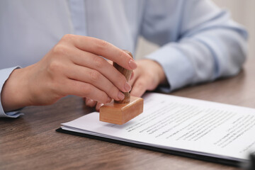 Wall Mural - Woman stamping document at wooden table, closeup