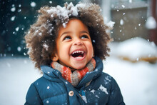 Young African American Toddler Laughing And Standing Outside In The Snow Catching Snowflakes In Hands, Wearing Gloves. Winter Snowing Cold Happy Holidays With White Christmas