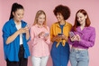 Group of beautiful multiracial women, smiling friends holding smartphone using mobile app shopping online ordering food, communication together isolated on pink background. Technology concept 