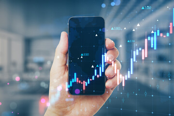 Wall Mural - Close up of male hand holding smartphone with glowing candlestick forex chart on blurry office interior background. Trade, finance and growing market concept. Double exposure.