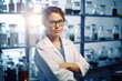 © vefimov - Professional woman wearing lab coat is standing in front of shelf filled with bottles. Scientist, researcher, or pharmacist in laboratory setting. Educational materials, healthcare publications