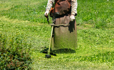 A man mows green grass with a petrol trimmer