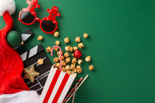 Christmas-themed Premiere Featuring Thematic Elements. Top-view Of Movie Clapper, Gingerbread Man-shaped Glasses, Delectable Popcorn, Santa's Hat, Ornaments, Straws On Green Backdrop With Ad Space