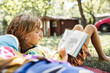© Westend61 - Blond boy reading book lying next to mother in forest