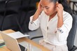 © Studio Marmellata - Side view of young Asian female manager in smart casual outfit sitting at table with laptop while adjusting headphones and listening to music during work