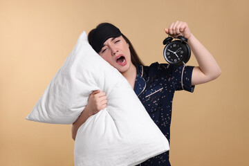 Canvas Print - Tired young woman with sleep mask and pillow yawning on beige background. Insomnia problem