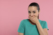 Embarrassed woman covering mouth on pink background. Space for text