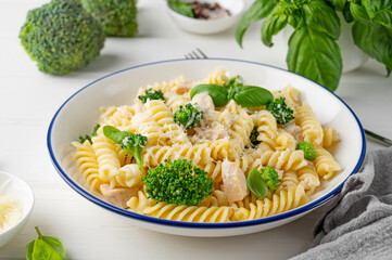 Wall Mural - Delicious broccoli and chicken fusilli pasta with parmesan cheese and fresh basil in a bowl on a white wooden background. Healthy comfort food.