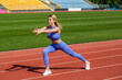 © Yevhen - Female runner stretching before workout. Sports exercises and stretching in the stadium. Physical training girl. Fit girl do outward lunging. Physical training education. Sports lesson
