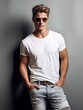 Junger Mann mit Sonnenbrille steht lässig an eine Wand gelehnt, mit weißem T-shirt und Jeans bekleidet