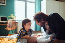 Loving Son And Father Playing With A Newborn Baby At Home