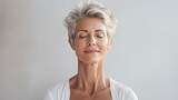 Fototapeta  - An elderly woman with grey hair with her eyes closed, meditates while doing Yoga. Zen mode, spiritual person