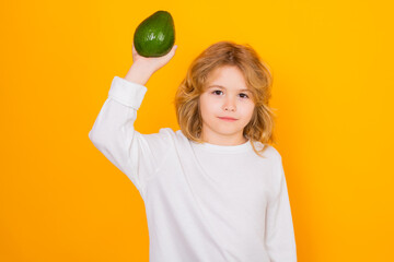 Wall Mural - Kid hold red avocado in studio. Studio portrait of cute child with avocado isolated on yellow background.