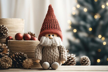 Close Up Of Handcrafted Christmas Gnome Knitted Figurine On Table Against Fir Tree In Living Room, Scandinavian, Nordic Dwarf With Red Hat. New Year Accent Decor In Home Interior.